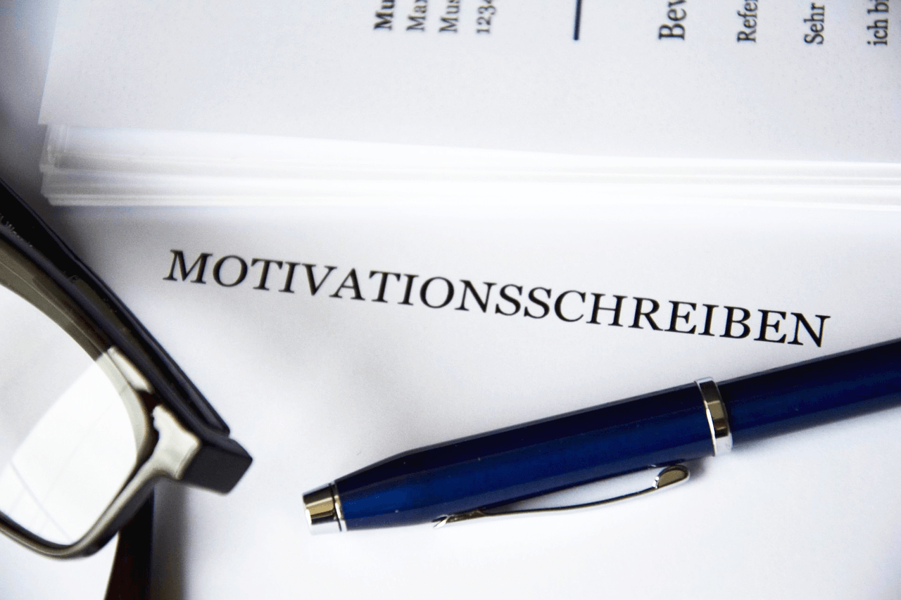 Das Bild zeigt den oberen Bereich eines Motivationsschreibens, mit Kugelschreiber und Brille. Im Beirag geht es darum, mit dem Anschreiben bei der Bewerbung zu punkten.